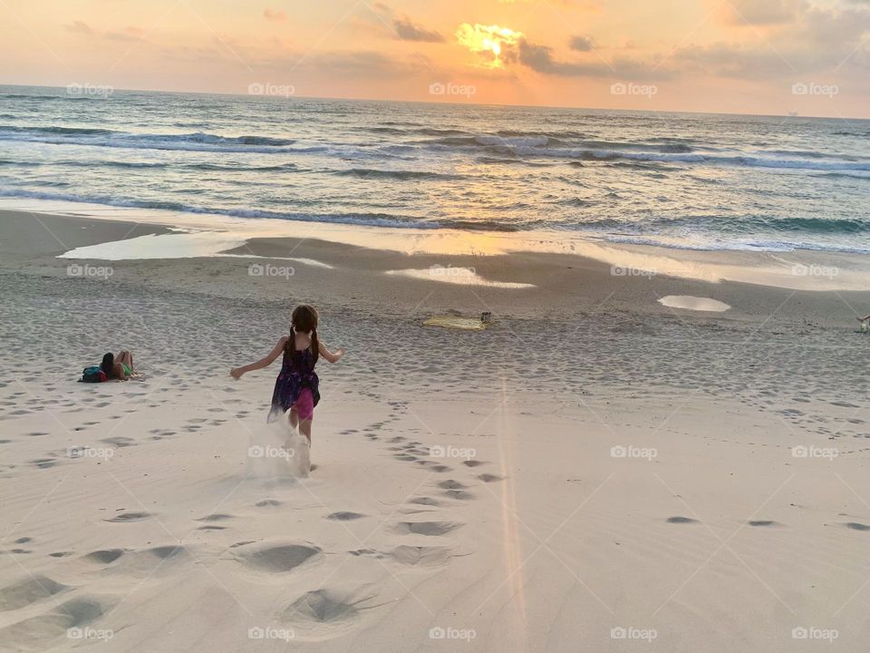 Girl running down the dune on the beach at sunset 