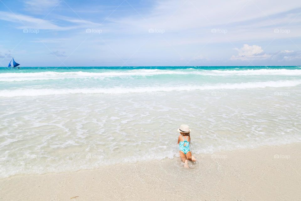 Happy little Caucasian girl with blonde hair having fun on sea at hot summer day 