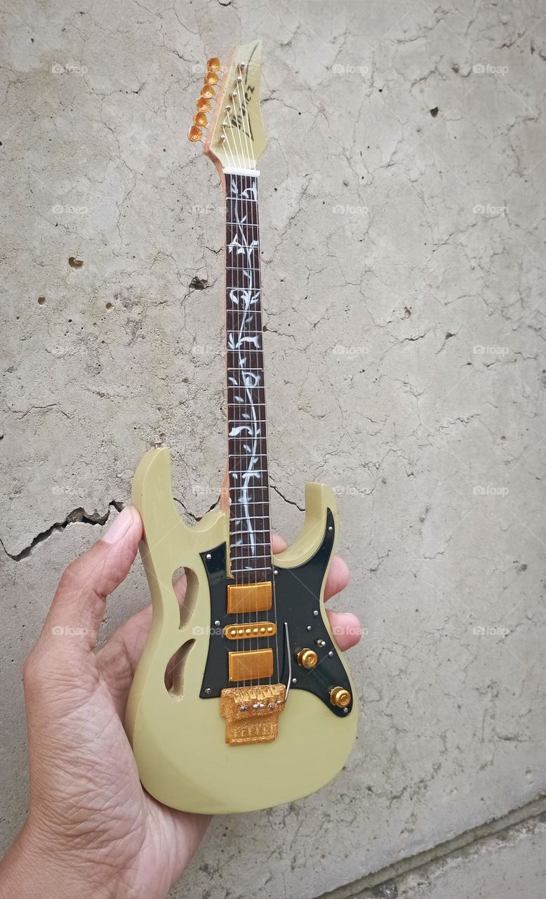 Guitar replica in a hand with concrete wall as background