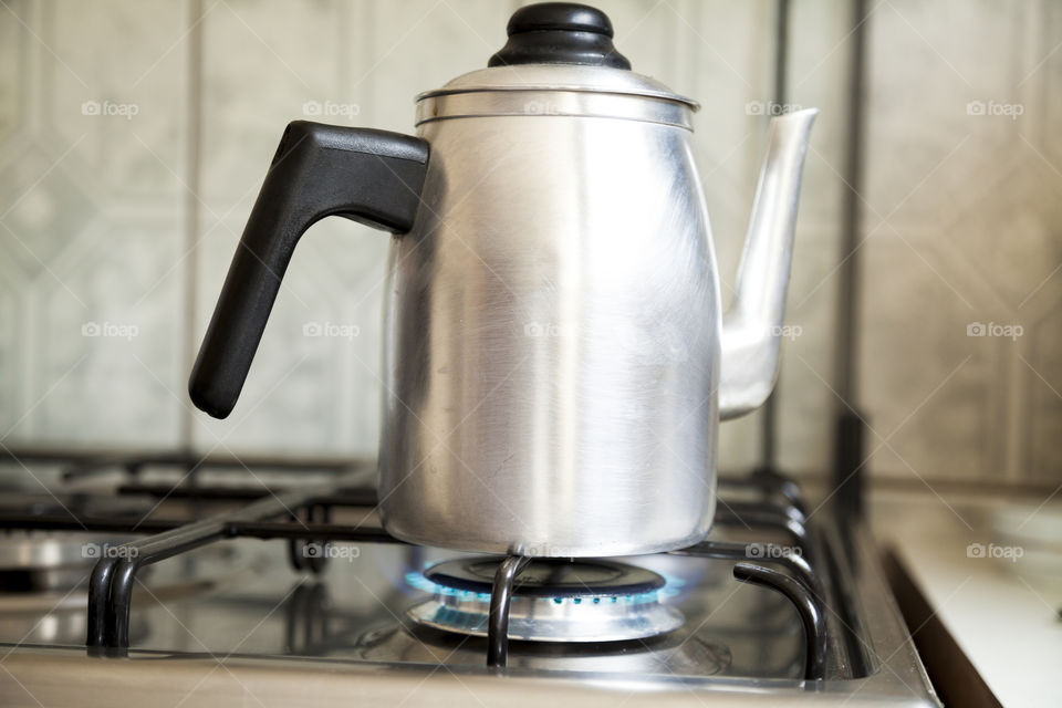 Coffee pot being heated on a residential stove over a low flame in a Brazilian house. Textured tile background in Brazilian cuisine. Copy space. Drink concept. Coffee concept.