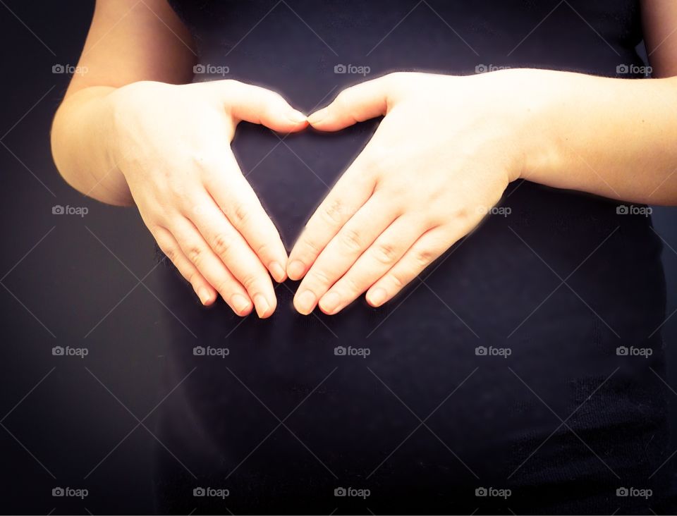 Midsection of pregnant woman forming heart shape on belly