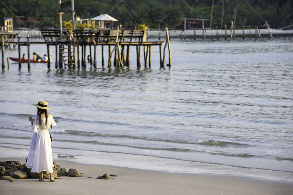 Asian woman playing phone on the beach  Background sea and a wooden bridge at Koh Kood, Trat in Thailand.