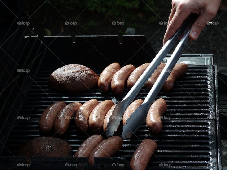 A person cooking hot dogs on a barbecue grill