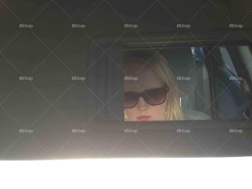 Women's reflection in car review mirror