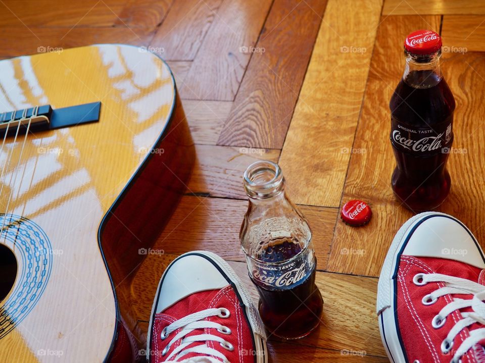 Coca Cola bottles on hardwood floor with red sneakers and guitar.