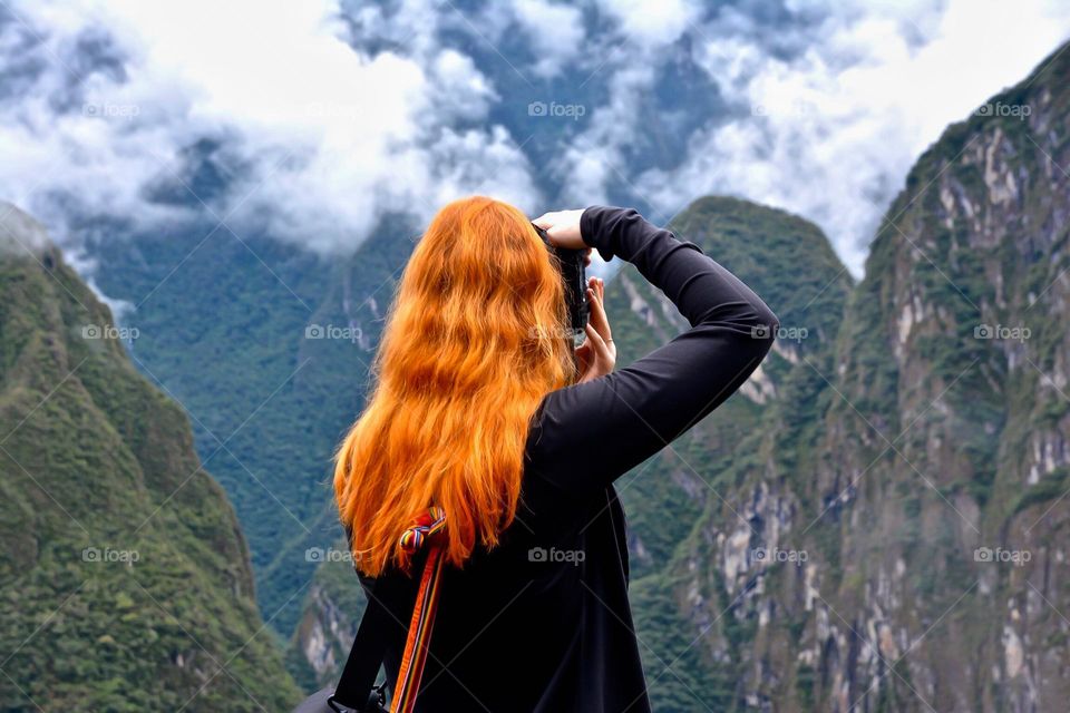 Red haired woman with camera shooting mountains