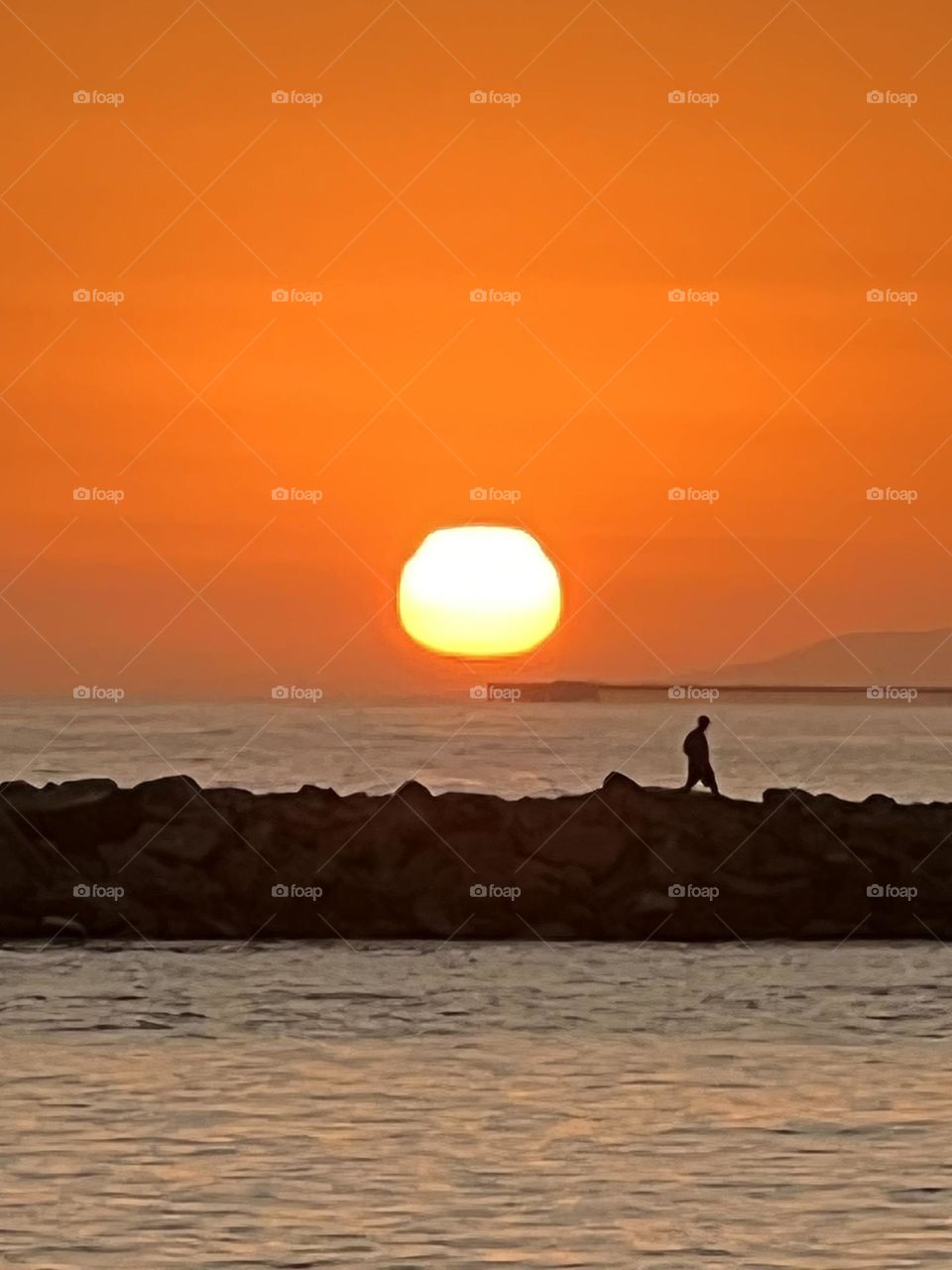 Beautiful sunset over the Newport Beach Jetty with a man walking in front of it