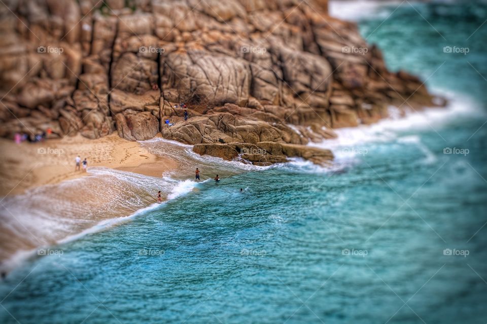 Porthcurno Cornwall. A sandy beach and rocky shoreline with emerald green sea taken from a birds eye view. Holidaymakers on the beach and sea