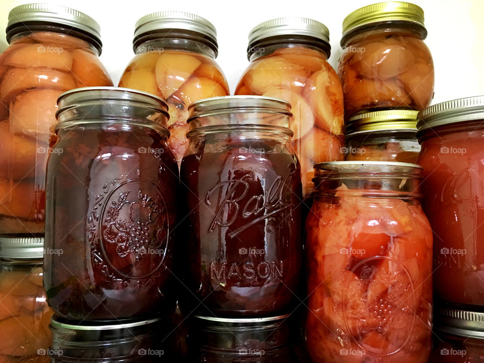 Closeup view of quart canning jars lined up on shelf filled with fruit preserves 