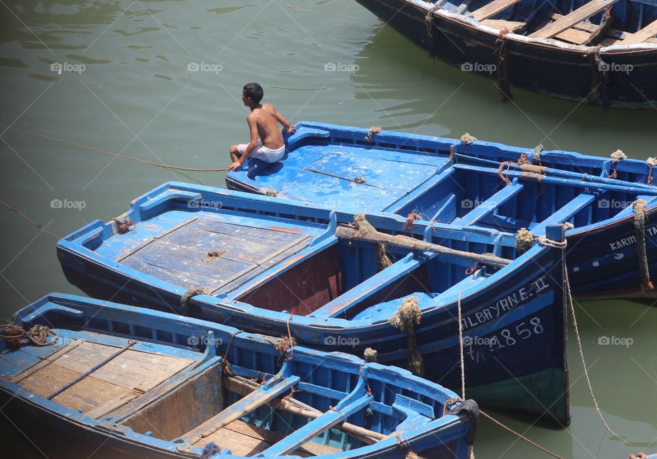 A boy sits on a fishing boat while taking a break from swimming 