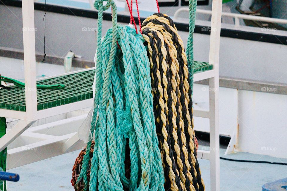 Commercial fishing vessel thick rope lines hanging neatly on the dock beside the boat, turquoise aquamarine color as well as braided