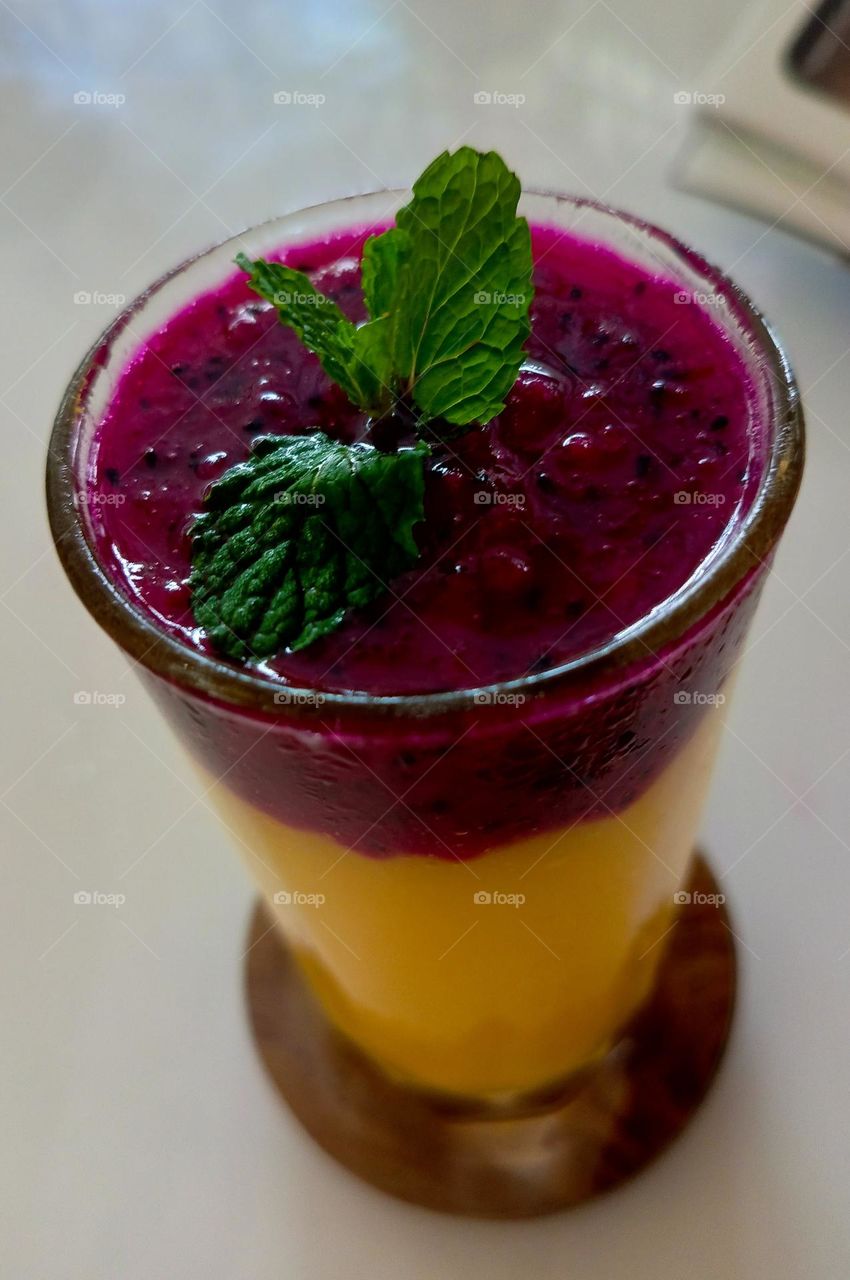 basil toping on the dragon fruit and mango juice is served in a glass.