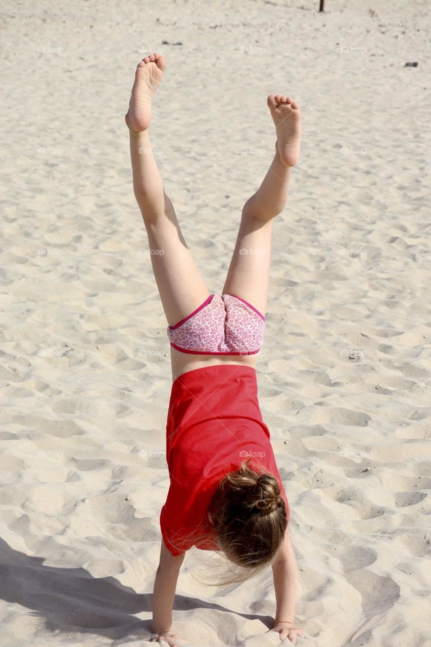 Little girl practicing handstand in sunny day