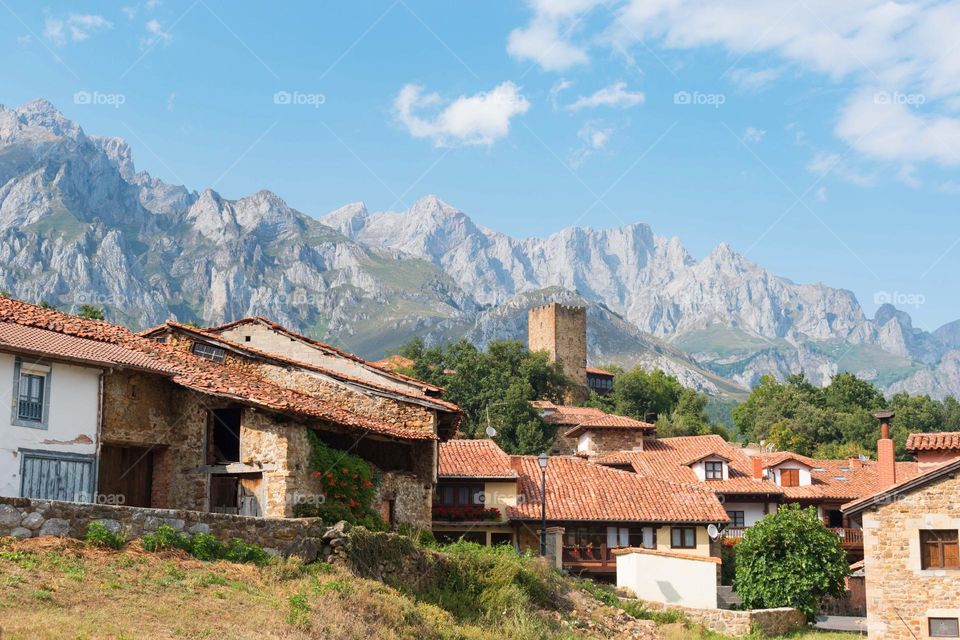 Panoramic view of a mountain village with traditional stone houses. A medieval old tower can be seen. Mountains (Picos de Europa) at the Background. Village of Mogrovejo, Cantabria (Spain)