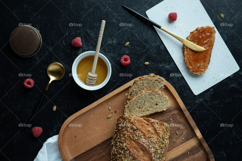 Flat lay of a loaf of bread on a wooden plate with a slice of toast and honey and jelly