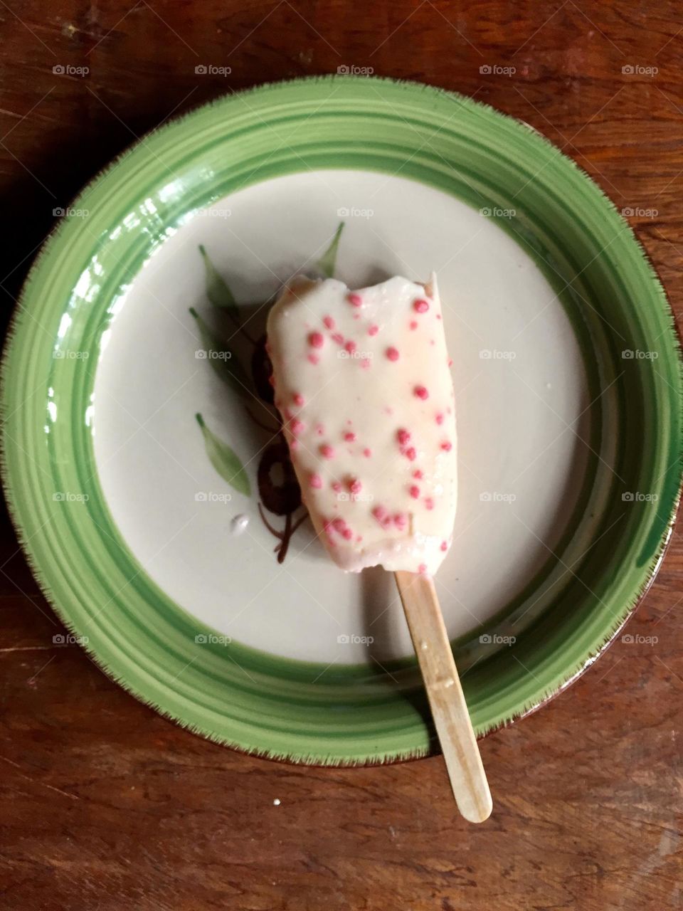 A melted ice cream on the stick. With strawberry flavor and put in a saucer.