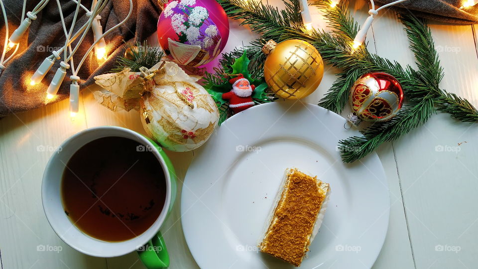 Christmas toys, a cup of hot tea, delicious Christmas garland cake on a white table