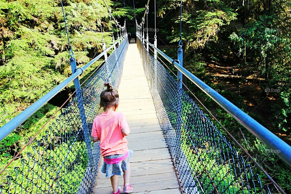 toddler girl crossing a suspension bridge.
