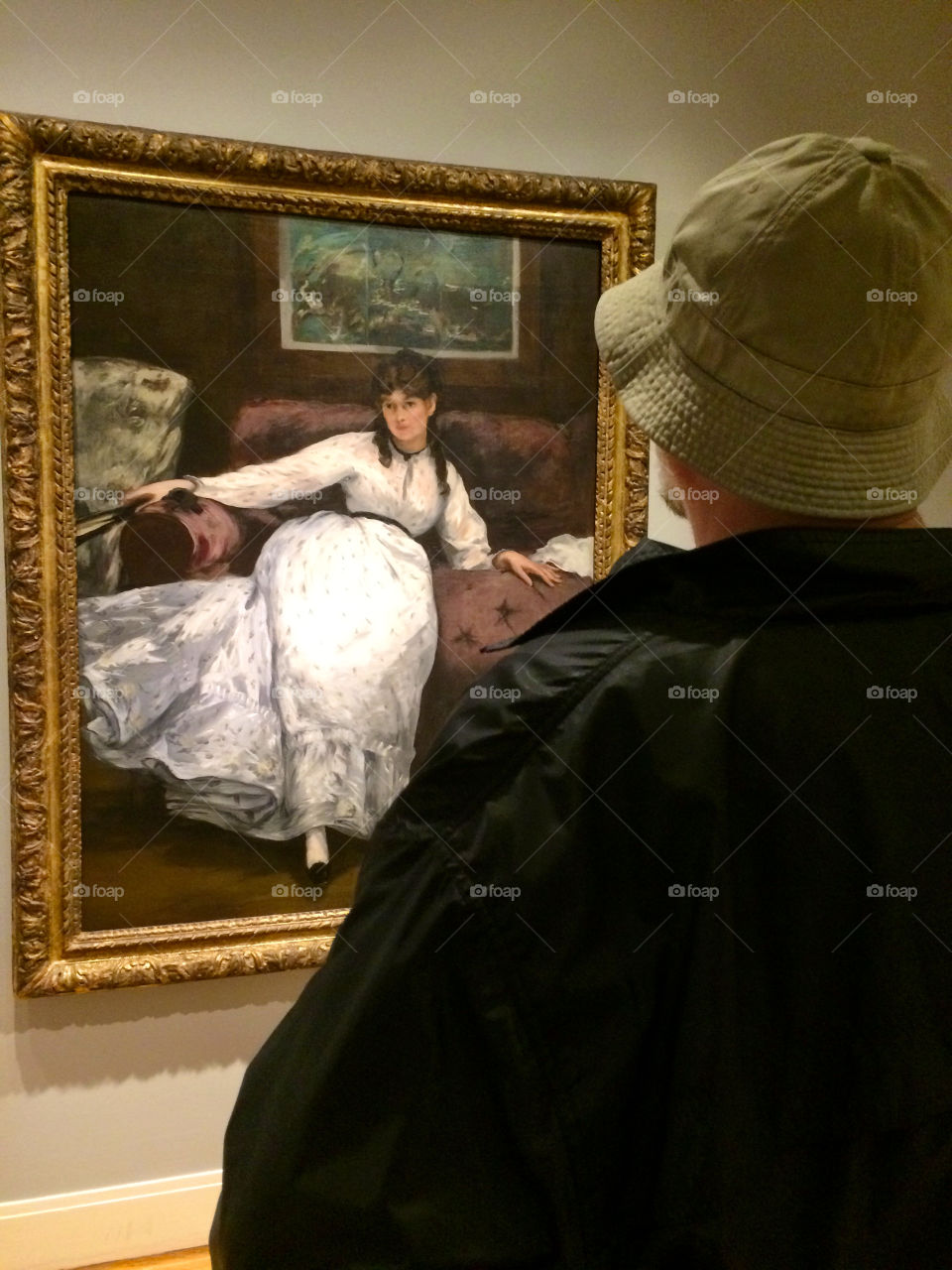 Man with hat stands infront of Manet painting. 