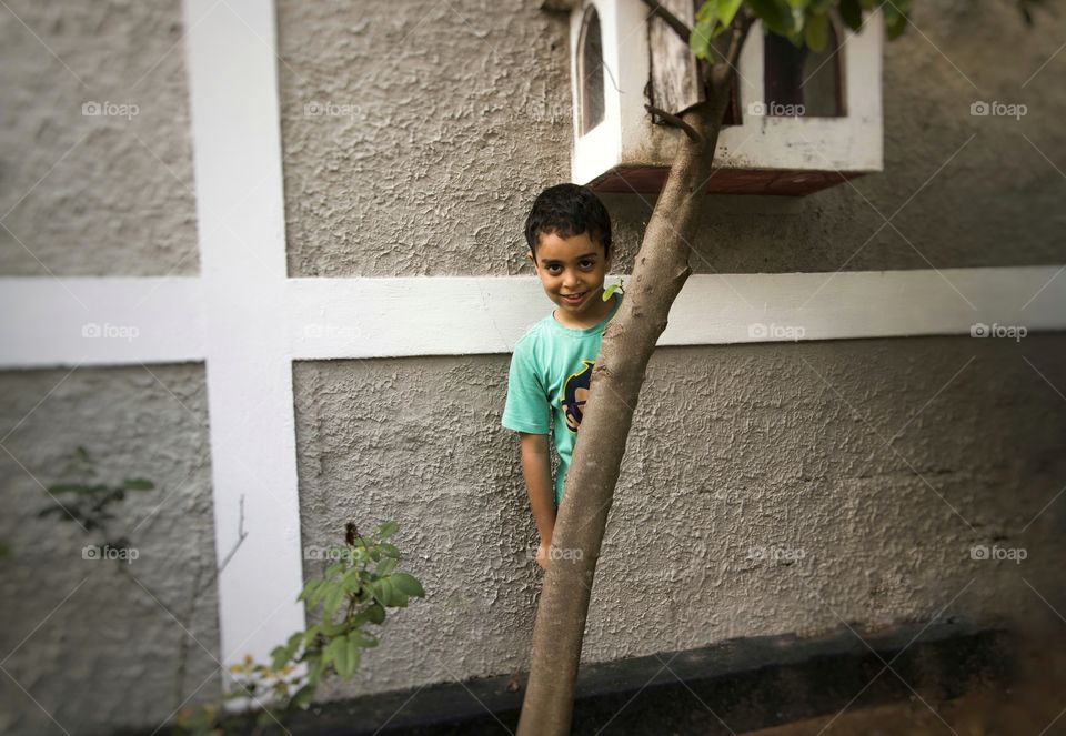 Smiling boy standing behind tree