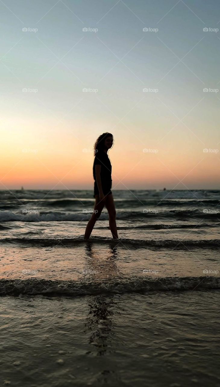young beautiful woman walking on the beach with the sunset in the background