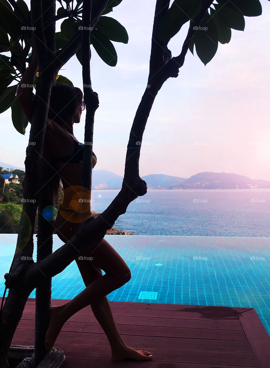 Silhouette of a young woman enjoying the evening view at the swimming pool above the sea 