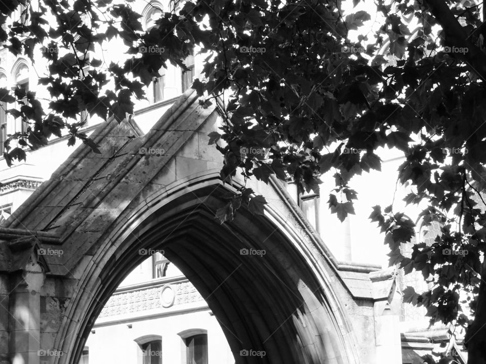 A stone archway entrance to an old European building on a sunny summer day with trees providing shade. 