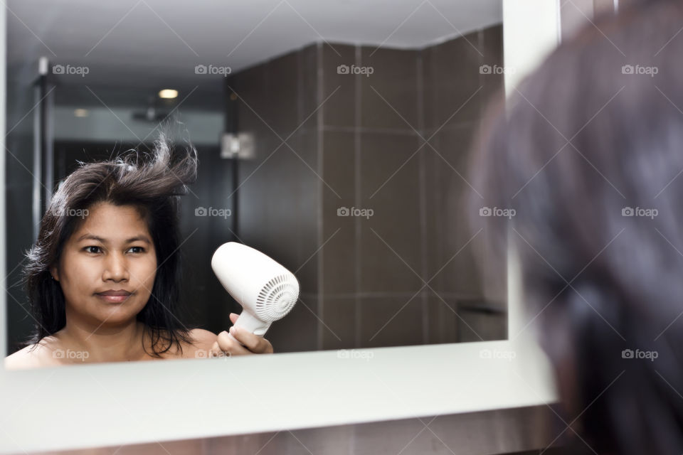 Asian lady drying her hair in front of mirror