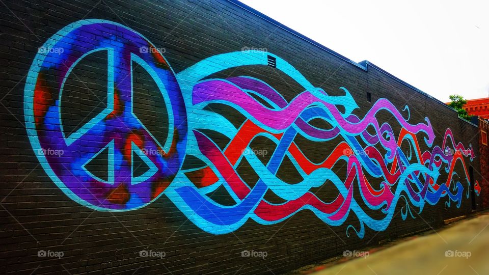 color love flying peace on a brick wall mural in blue red pink and black in an urban setting