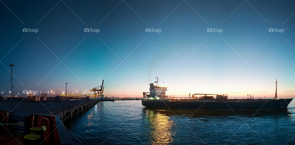 Panorama view of a tanker vessel departing from the port during a beautiful sunset with a clear blue sky.