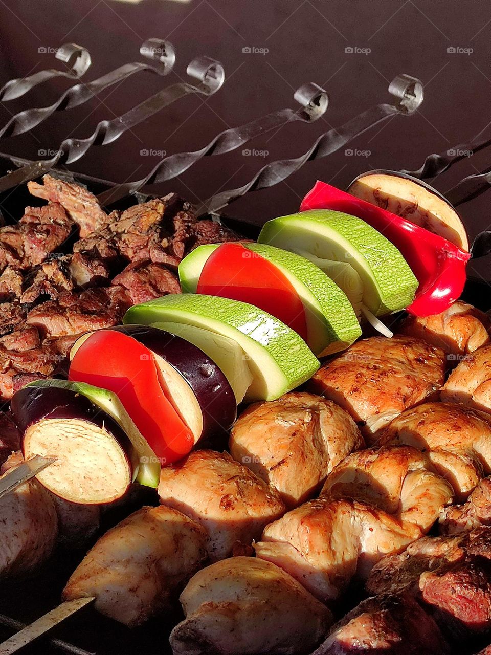 Grill. Grilled meat on metal skewers. Rings of purple eggplant, red bell pepper, green zucchini and onion are strung on one skewer. Appetizing natural colors of vegetables