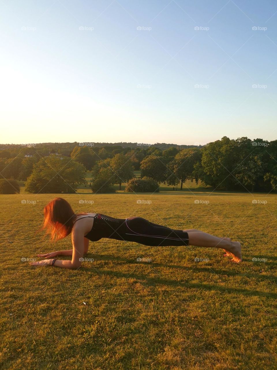 Yoga time in the park. Women does yoga. Sports lifestyle. Exercise "plank". Red colour hair. Healthy lifestyle. 
Unusual shooting angle. Shooting from below. Down up. From the ground up...