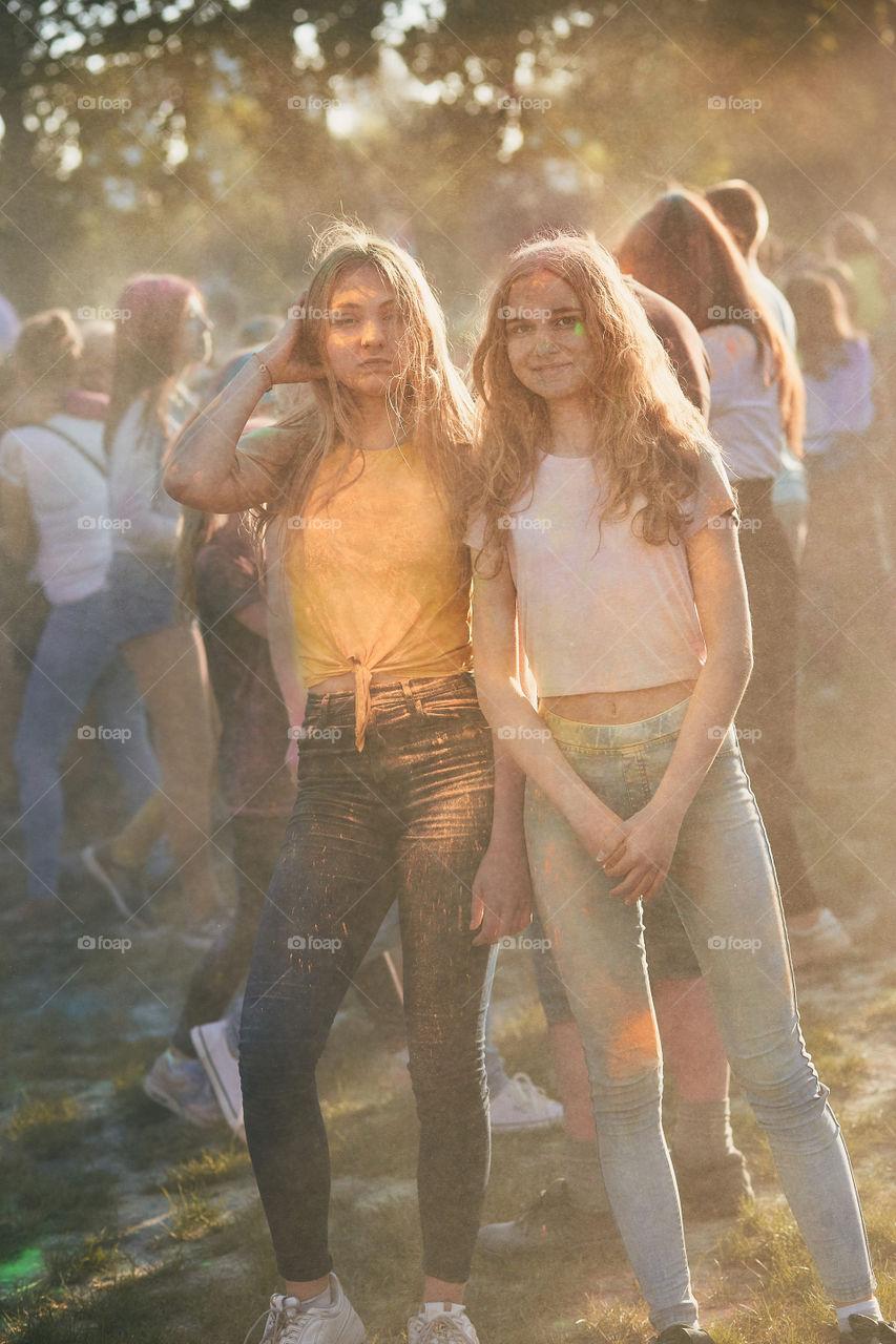 Portrait of happy smiling young girls with colorful paints on faces and clothes. Two friends spending time on holi color festival. Real people, authentic situations