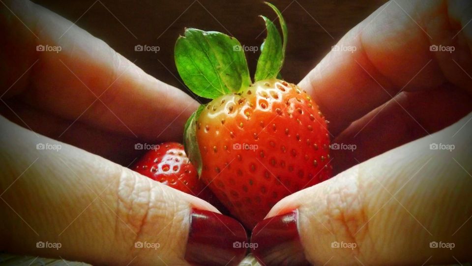 Hands with red nails holding strawberry