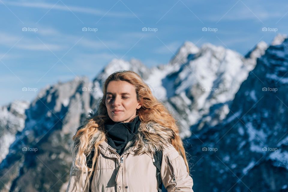 Happy young woman enjoying cold fresh air while hiking in the mountains on a sunny day in winter