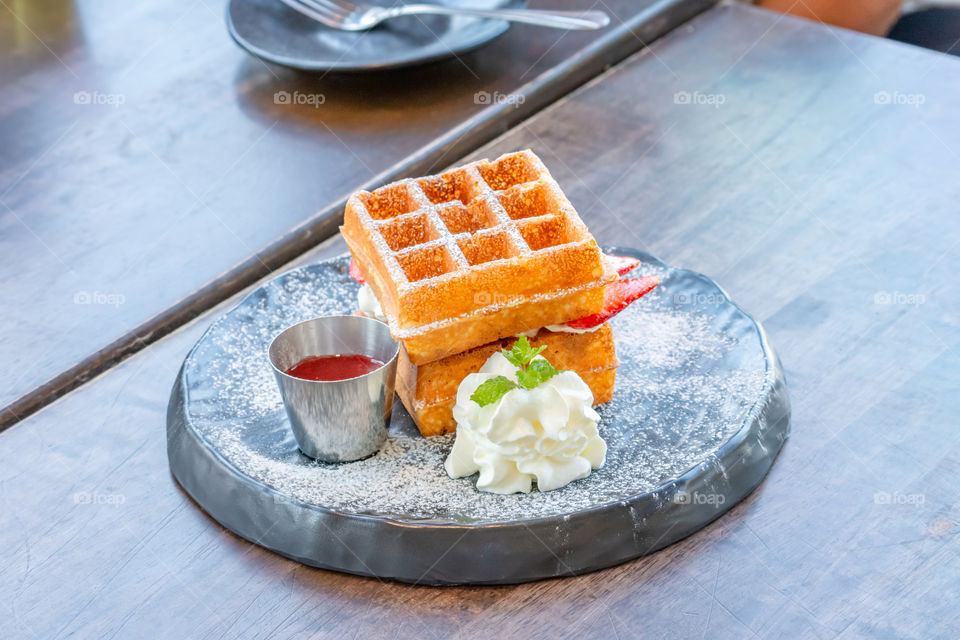 Waffle Strawerry fresh cream in the black plate on wooden table.