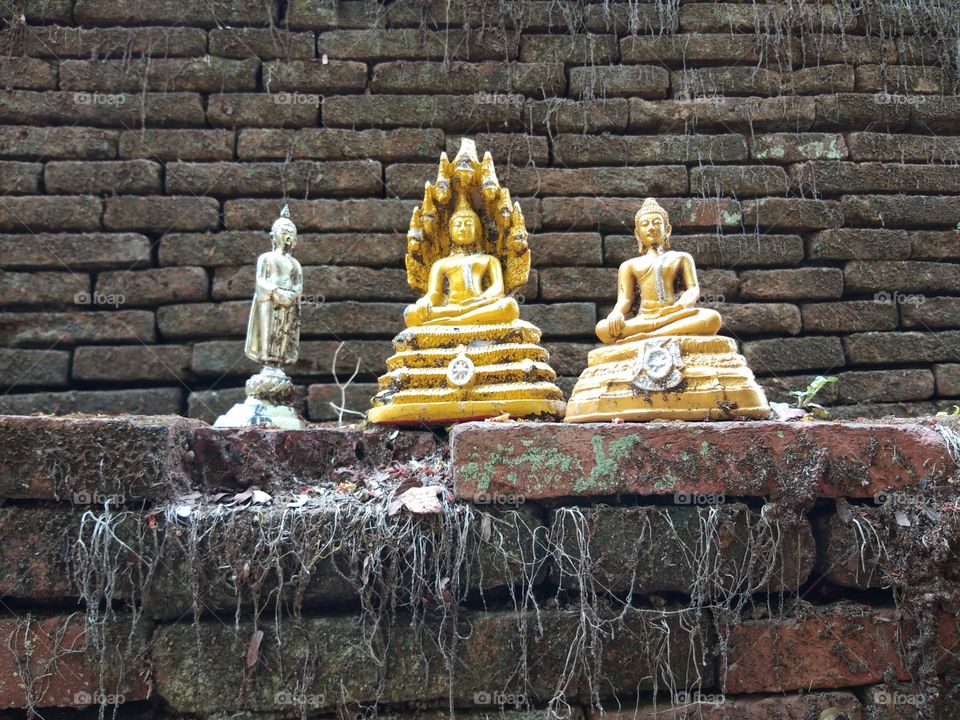 The ancient Buddha statue on the old brick wall at the northern Thai temple.