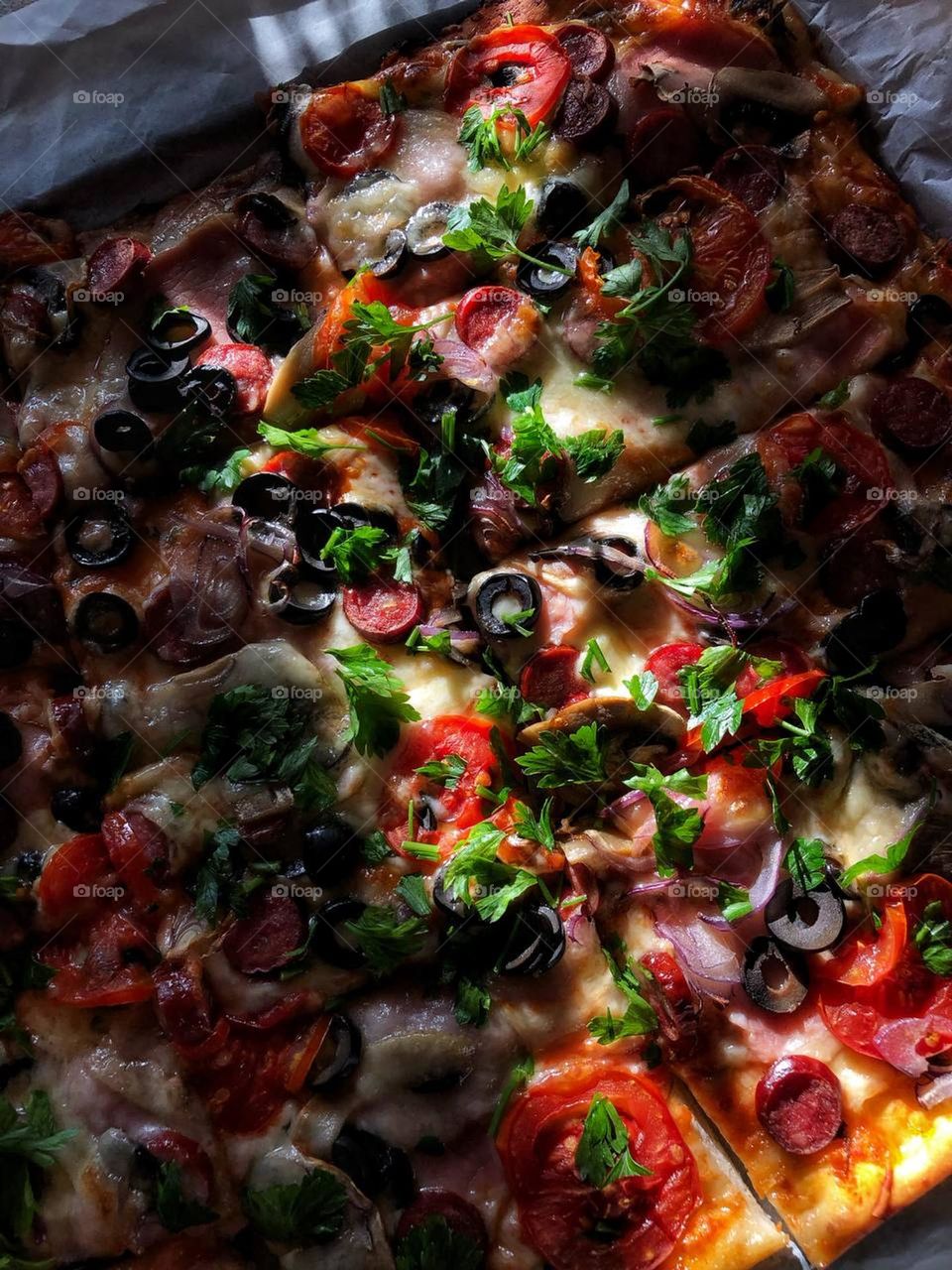 macro photo of homemade pizza with sausage, cheese, olives and greens