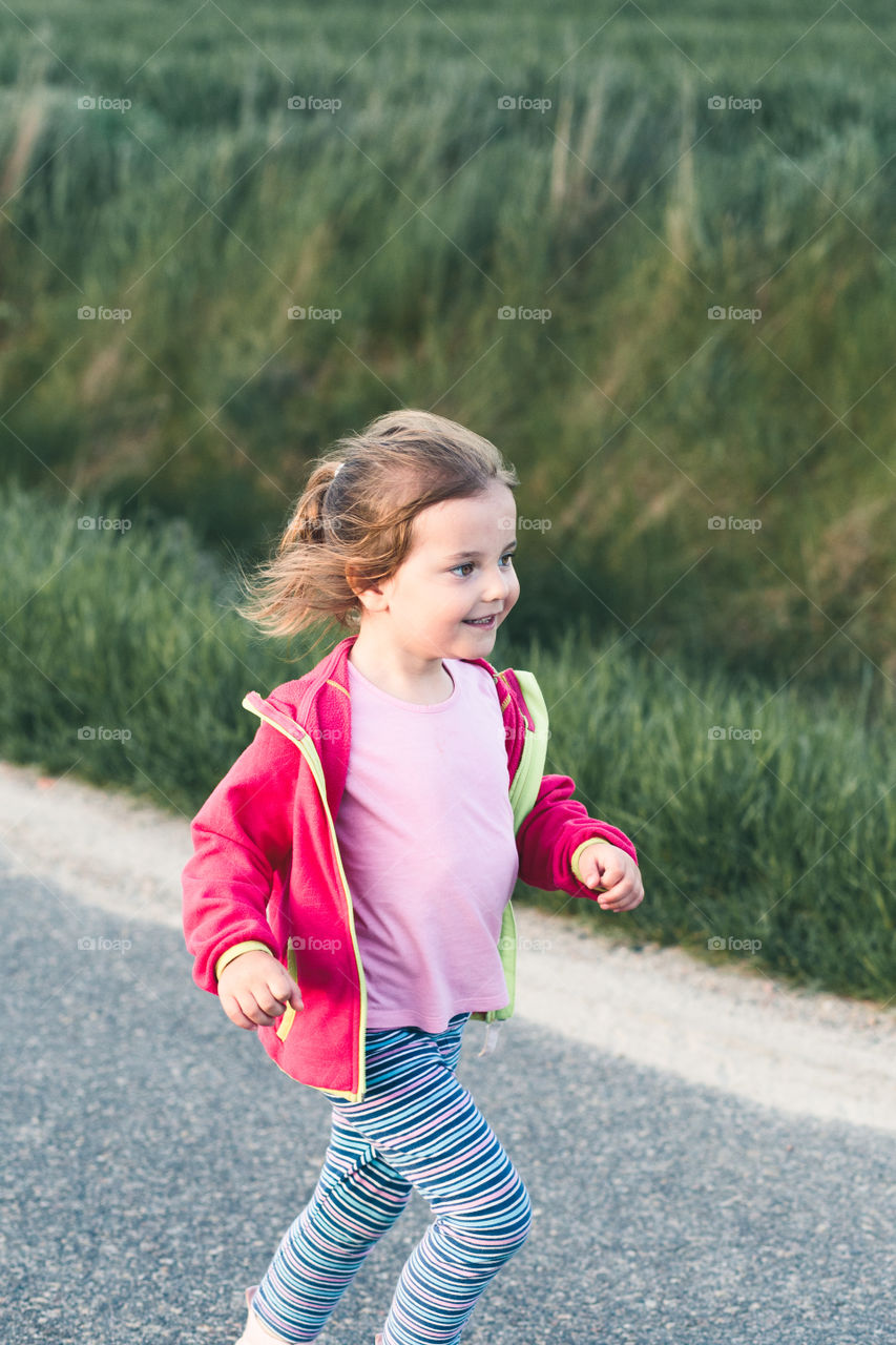 Little adorable girl having fun running on road, playing outdoors