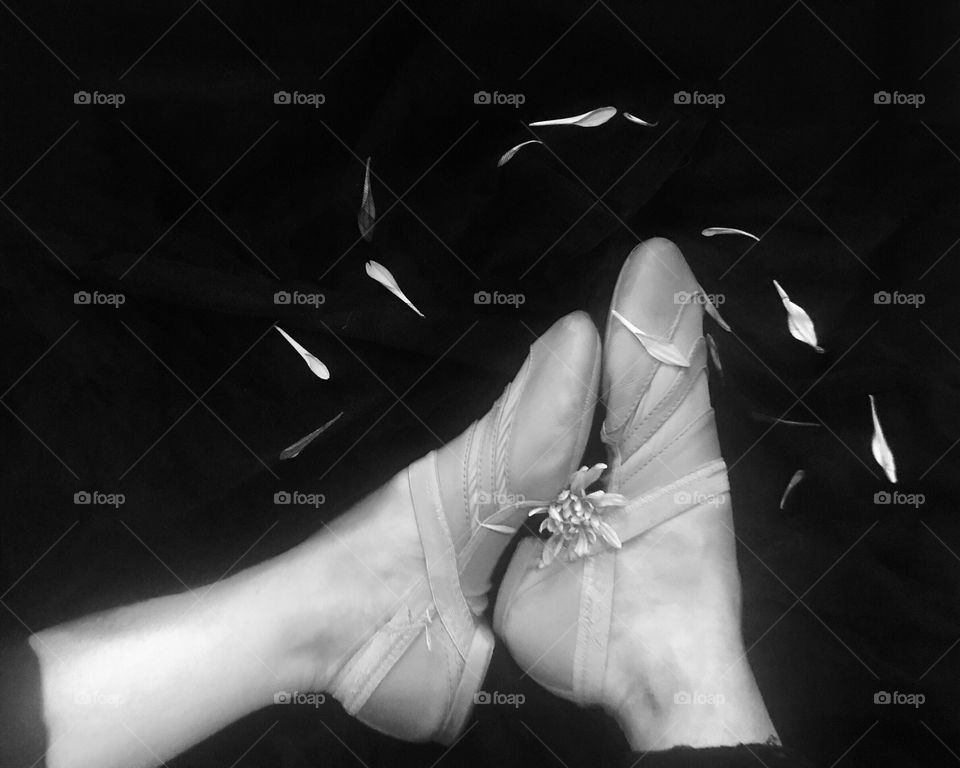 A black and white photograph of a girl wearing jazz dance ballet shoes with flower petals surrounding her feet. 