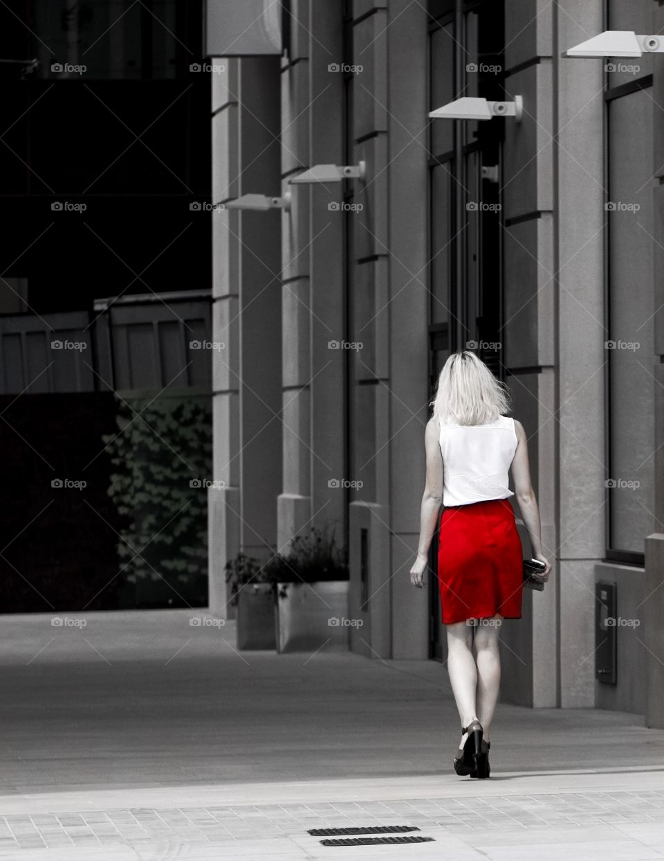 A single woman with a red skirt walking alone down a deserted alley way.