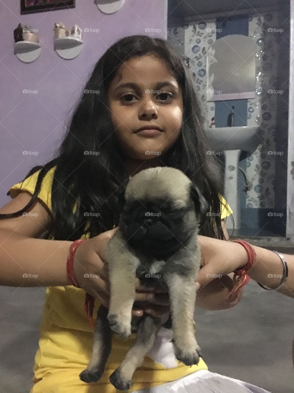 A cute little dog in the hands of cute little angel.Both are looking great.A great bond shows in between them 