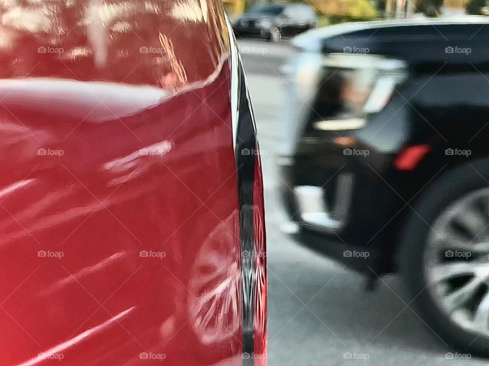 Commuting: reflection of a black vehicle driving behind the red pickup truck back by the ride side light in a parking lot, close-up.