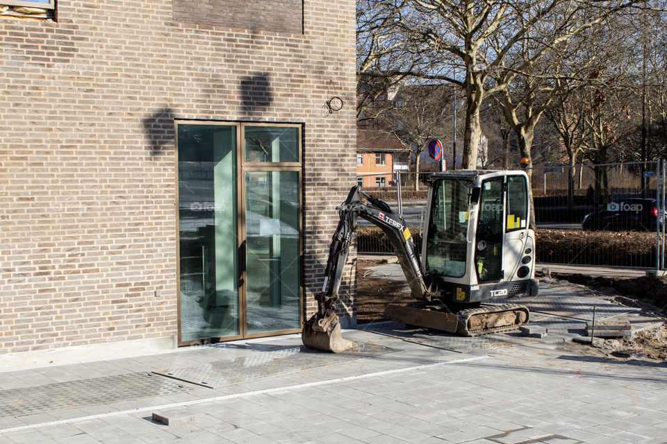 Construction machine digger, next to newly build glass panel in newly build building