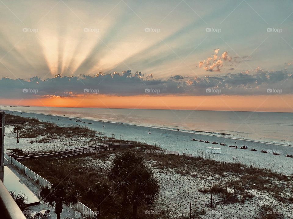 Daybreak over the Gulf of Mexico in the United States. The rising sun is behind a low clouds as rays illuminate the sky.