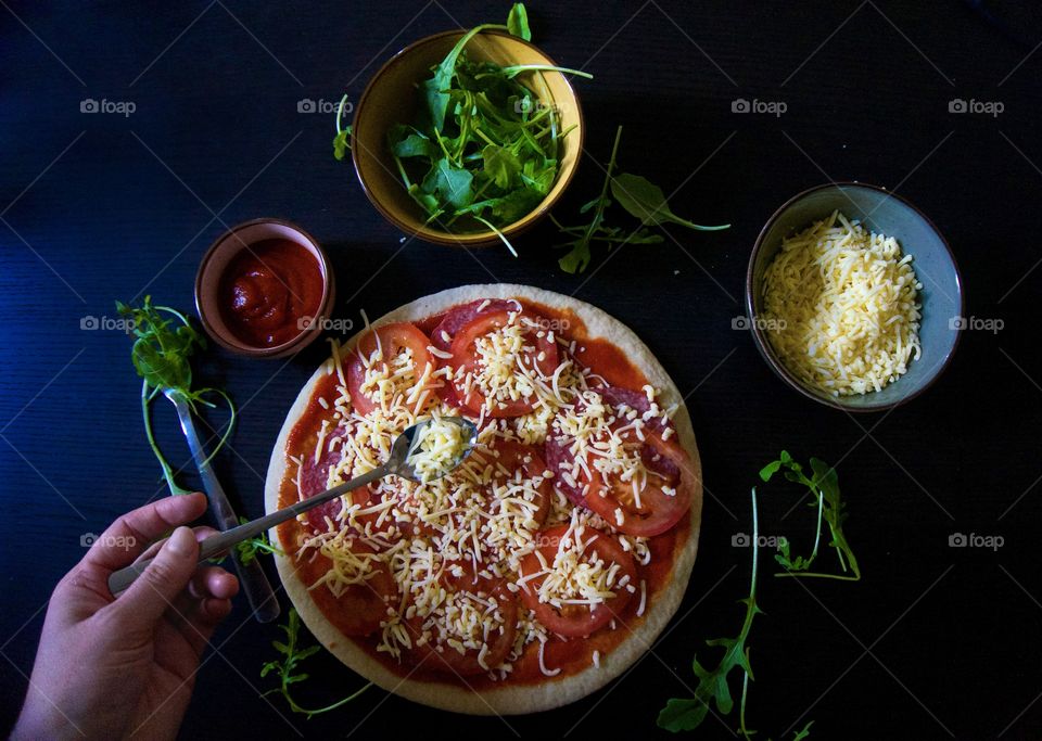 Making a pizza at home with cauliflower dough, tomato sauce, cheese and salami