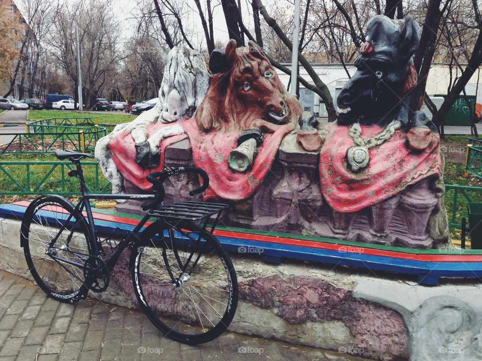 Grayish-black brakeless fixie bicycle standing near sculpture with three horses heads