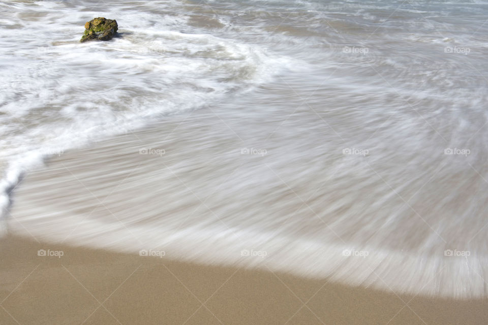 A close up view of the long exposure of the swirling and white surf moving over the tan sand!