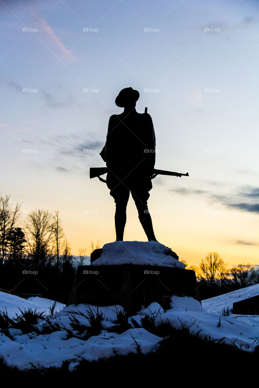 Silhouette of the statue of a soldier holding a rifle. Memorial, war, sunset related picture.