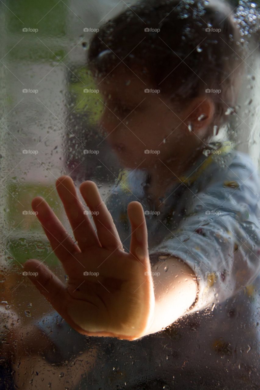 sad portrait of a boy through wet glass